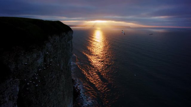 Mid summer Sun Set over coastal bay with sea birds coming in to roost on cliff edge. Sounds of waves on the shore and bird song.