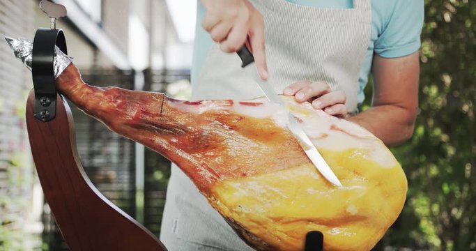 Man cutting off lard from the whole jamon leg or dry-cured ham. Shot on Red