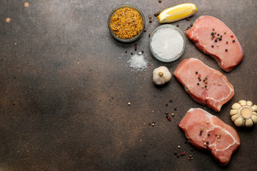 Raw pork steak, meat and ingredients for cooking, spices, herbs and vegetables on a dark background. top view. space for text