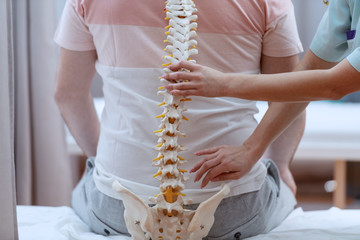Caucasian nurse holding spine model against the patients backs. Clinic interior.