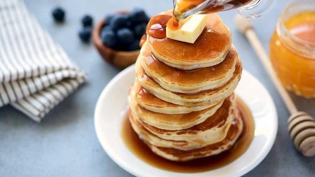 Slow motion of pouring syrup on stack of pancakes with butter. Tasty breakfast food