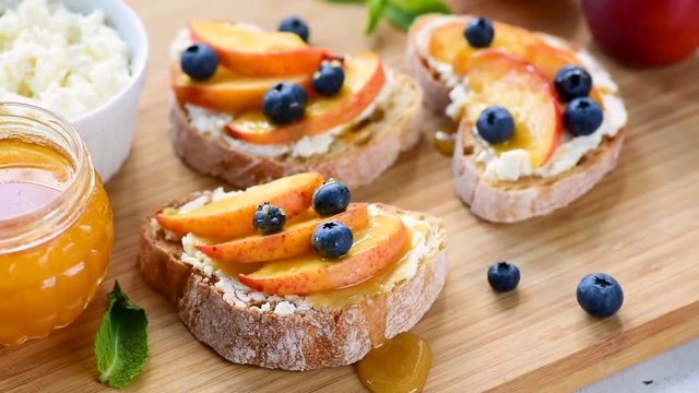 Tasty fruit bruschetta with ricotta cheese, peach, blueberries and honey on wooden serving board. Healthy appetizer, breakfast or snack