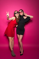 Young pretty two women in dressed have fun, dance, scream while standing isolated on crimson background