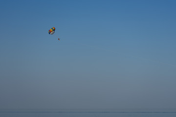 A multi-colored parachute over the sea against a clear blue sky.