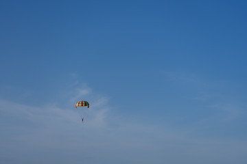 A multi-colored parachute over the sea against a clear blue sky.