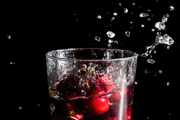 Splash of cherries dropped in a glass of water. Close up macro in studio for wallpaper.