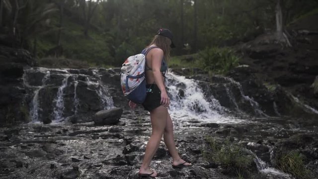 Slow Motion: Young Woman in Bikini Walks Across Waterfall Rocks, Kauai, Hawaii