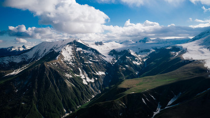 Aerial view of beautiful mountainous range and valley in Georgia. Mountains with snowy tops, blue sky, clouds.