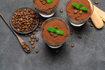 Classic tiramisu dessert in a glass and savoiardi cookies on dark concrete background