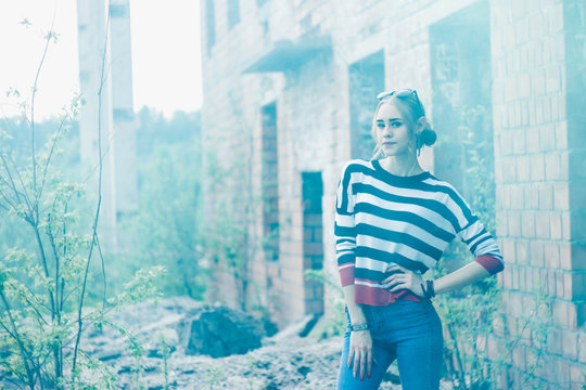 Blonde in a striped jacket on the background of a brick building and trees with a green smoke bomb