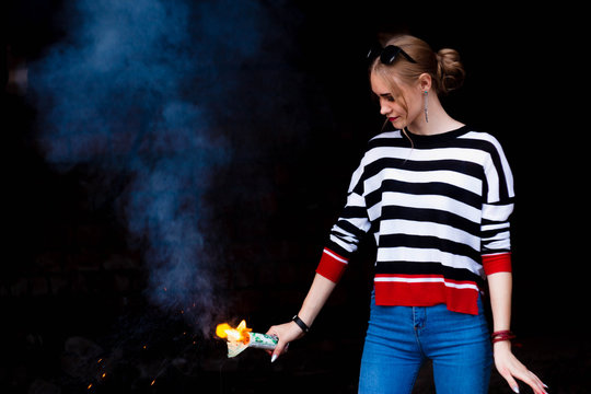 Blonde in a striped jacket on the background of a brick building and trees with a green smoke bomb