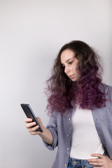 Fototapeta premium Young girl thoughtfully looks in phone. Curly color coloring purple hair. Gray background
