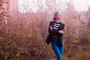 Blonde in striped jacket against brick building and trees in pink smoke