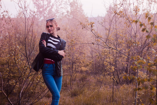 Blonde in striped jacket against brick building and trees in pink smoke