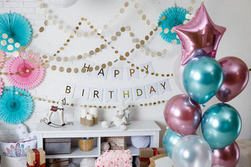 Garland with the inscription happy birthday. Birthday pink and teal decorations with gifts, toys, garlands and candy for yearling little baby party on a white bricks background.