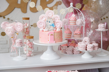 Beautiful birthday cake with pink decor for the birthday of a yearling child. Candy bar with cupcakes, marshmallows, cakes, meringues.