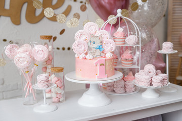 Beautiful birthday cake with pink decor for the birthday of a yearling child. Candy bar with cupcakes, marshmallows, cakes, meringues.