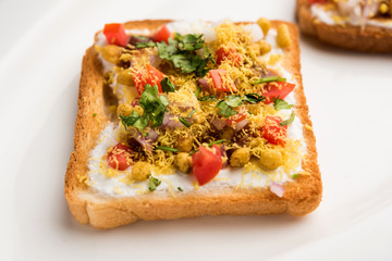Bread ppadi chaat/chat is a yummy starter/appetizer from India, served in a plate garnished with tomato, sev and coriander and masala. selective focus