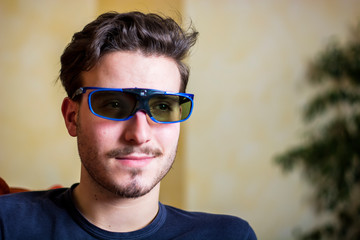 Young man in 3d glasses sitting on a sofa in the living room watching reality television leaning...