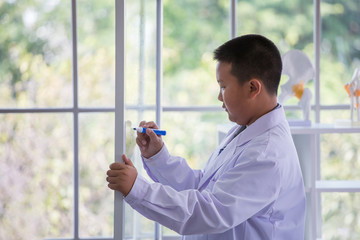 Pupils boy in white gown doing a chemical experiment write on glass board in laboratory at school  . kids in science lab study . multi ethnic . asian , biochemistry .