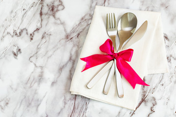 Flat lay - cutlery, spoon fork and knife on a rustic napkin and a bow of silk ribbon lie on a marble table, copy space.