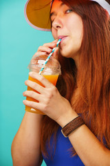 Woman wearing a blue swimsuit and hat drinks fruit juice from a cup