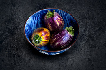 Healthy and fresh purple eggplants in a bwols over dark stone background. Vegetarian food, health or cooking concept.