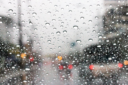 The windshield has rain water on the road when driving on the city streets.
