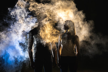 The man and woman standing near the smoke in the dark