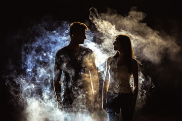 Obraz premium The couple standing near the smoke in the dark