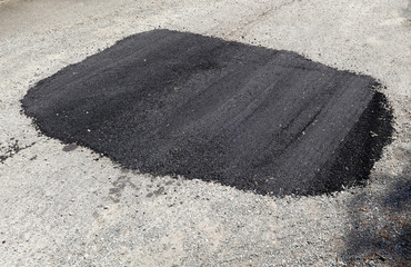 New asphalt repair of pothole on city street.