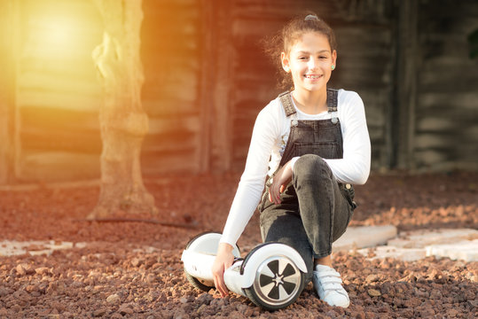Beautiful kid Smile with Braces.Young hipster teenager girl sit with electric Hover Board, Dual Wheel Self Balancing Electric Skateboard at the sunny park, child using two-wheeled board. Copy space.