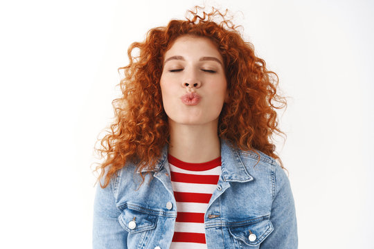 Close-up romantic cute feminine silly redhead girl curly hairstyle prepared lips kiss folding mouth close eyes wanna receive muah standing white background express love tenderness and sympathy