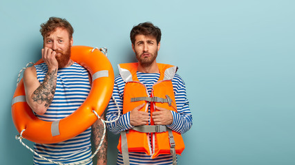 Sad professional rescuers face problem, cannot save drowning person, look dejected and nervous, pose with inflated lifering, wear protective lifejacket, pose indoor. Accident prevention on water