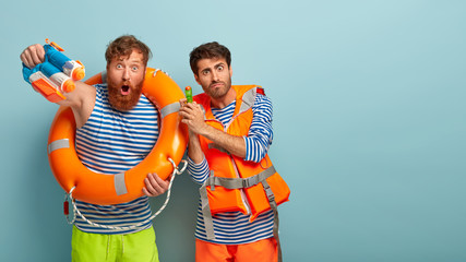 Horizontal shot of surprised Caucasian men hold squirt guns, spray water have real fight at summer...