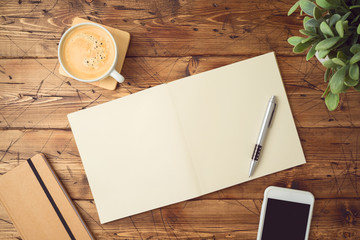 School notebook with coffee cup, smartphone and plant on wooden table.