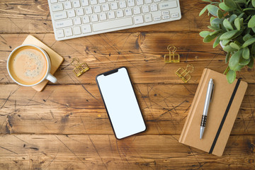 Smartphone mockup template with coffee cup and notebook on wooden table. Top view from above