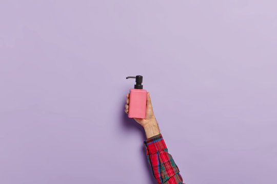 Photo of male hand with spray bottle of anti bacterial liquid soap for washing hands. Man going to apply moisturizing sanitizer. Disinfection and hygiene concept. Isolated on purple background.