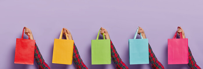 Image of mans hands with various colorful shopping bags isolated on purple background. Black Friday. Consumerism, sale, shopping and purchasing concept. Unknown male customer with many packages