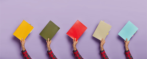 Collage image of various colorful textbooks in male hands isolated over purple background. Books...