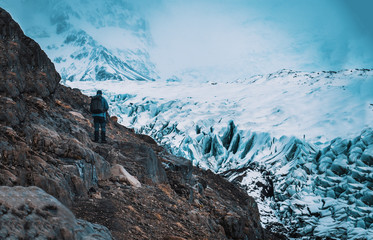 Back view of professional mountaineer in warm clothes walking on icy surface glacier by snowy mountain in Iceland