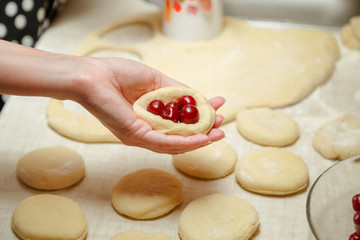 Cooking cherry pies in the home kitchen. Women's hands in the process of cooking cakes with cherries.