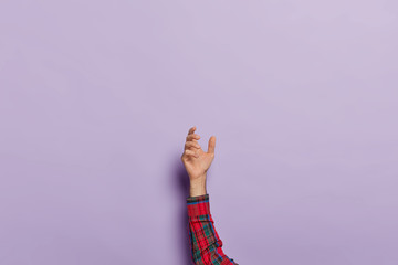 Raised male hand holding invisible object or item against purple background. Close up shot of arm with empty space for placing mobile phone or other virtual thing. Man picks up something above