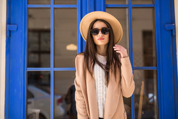 Young pretty woman woman wear in coat and hat with smile stands at the blue door on the street