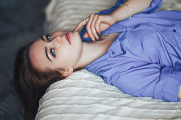 Sexy young beautiful woman with blue big eyes lond hair lying on bed at home in blue shirt