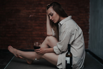beautiful sad woman sitting on floor in shirt, hold wine she is upset, alone, nobody loved, without love