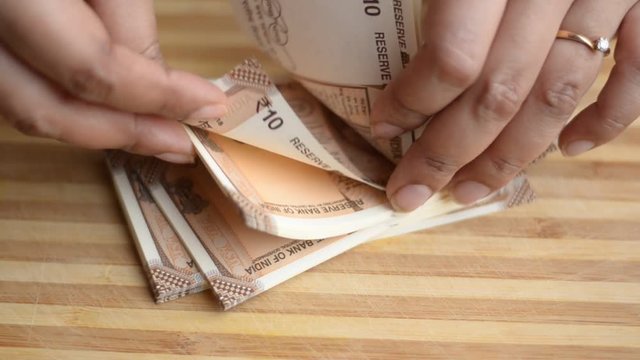 Hands counting new brown Rs10 Indian Rupees Currency notes against a wooden board background