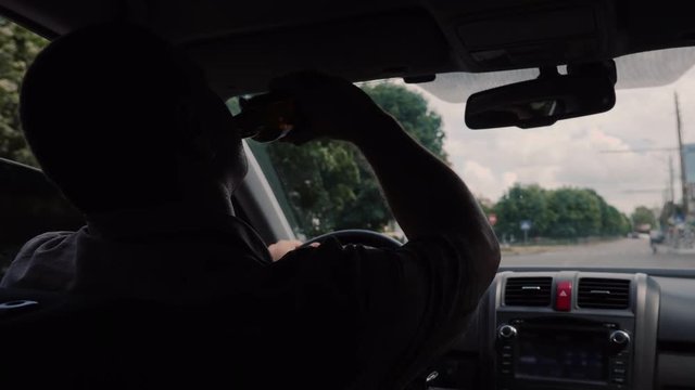 Rear view of driver drinks alcohol at the wheel. Dangerous illegal behavior concept