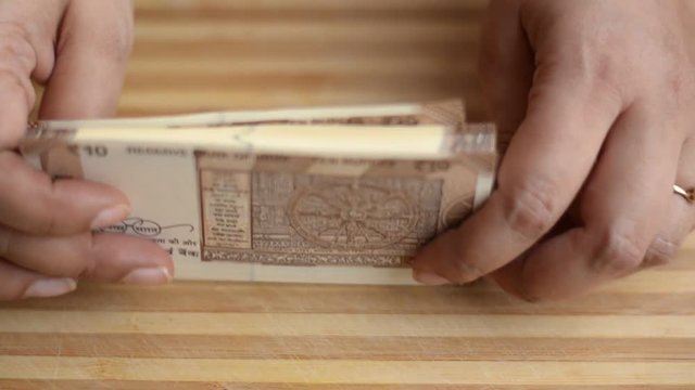 Hands counting new brown Rs10 Indian Rupees Currency notes against a wooden board background and arranging them