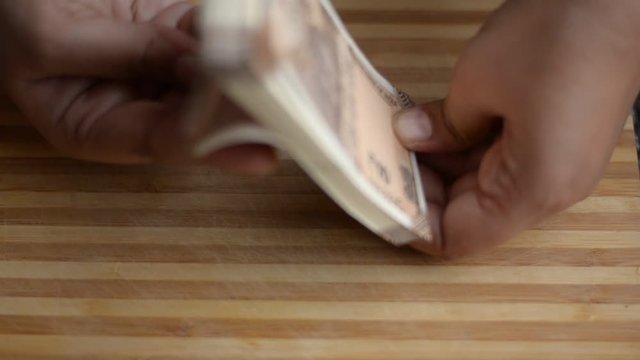 Hands counting new brown Rs10 Indian Rupees Currency notes against a wooden board background